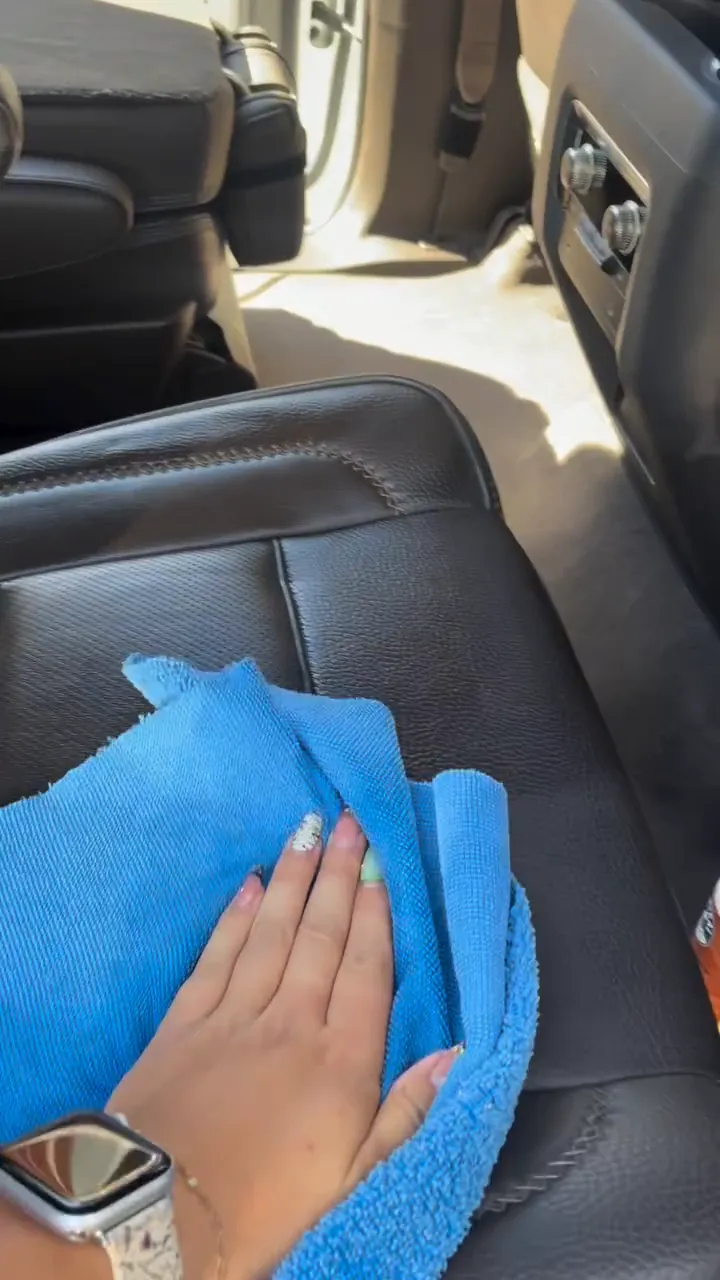 Wiping a black leather seat with a blue microfiber towel